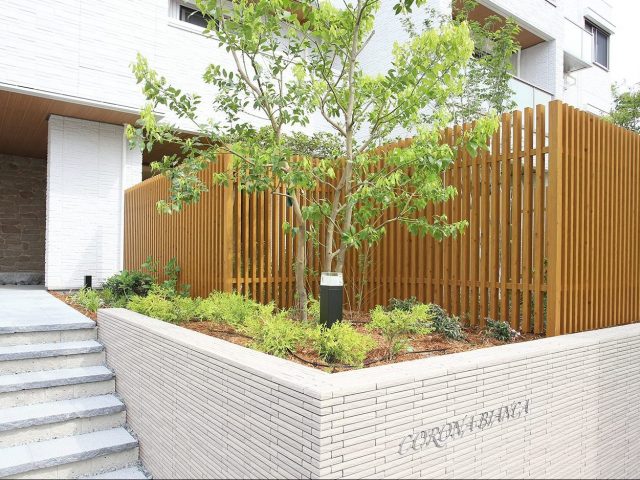 木目調のアルミ製格子フェンス。リバーシブル仕様で表裏もすっきり、植栽の緑ともよく調和します